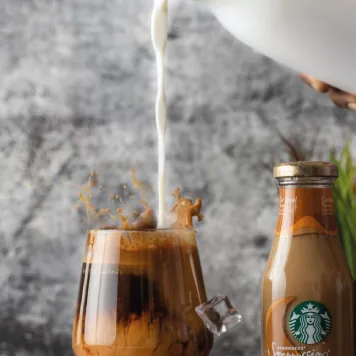 Milk being poured into iced coffee beside a Starbucks bottle